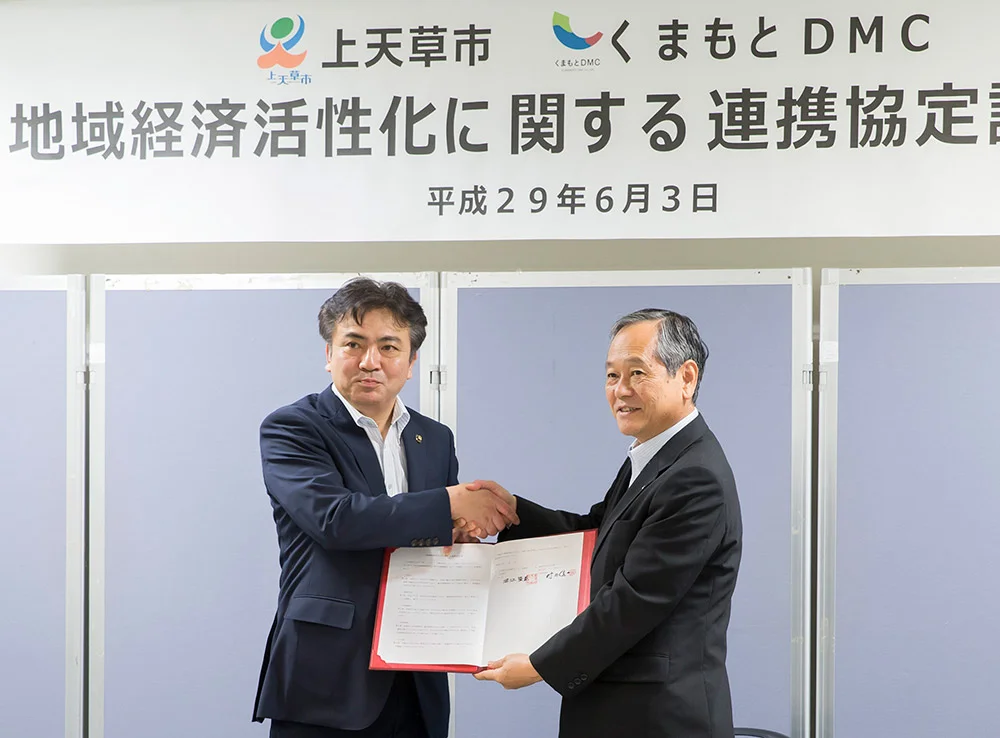 代替テキスト: 上天草市とくまもとDMCの「地域経済活性化に関する連携協定」調印式で、協定書に署名する上天草市の堀江隆臣市長(左)と、くまもとDMCの村田信一代表取締役社長(右)