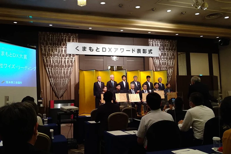 くまもとDXアワード表彰式で壇上に並び賞状を持つ受賞者たち